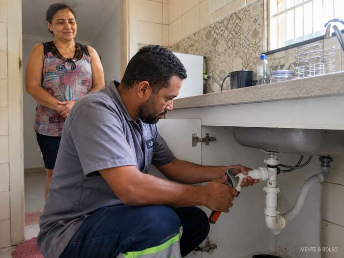 Mulher sorrindo, sentada tranquilamente no sofá de casa olhando para o celular