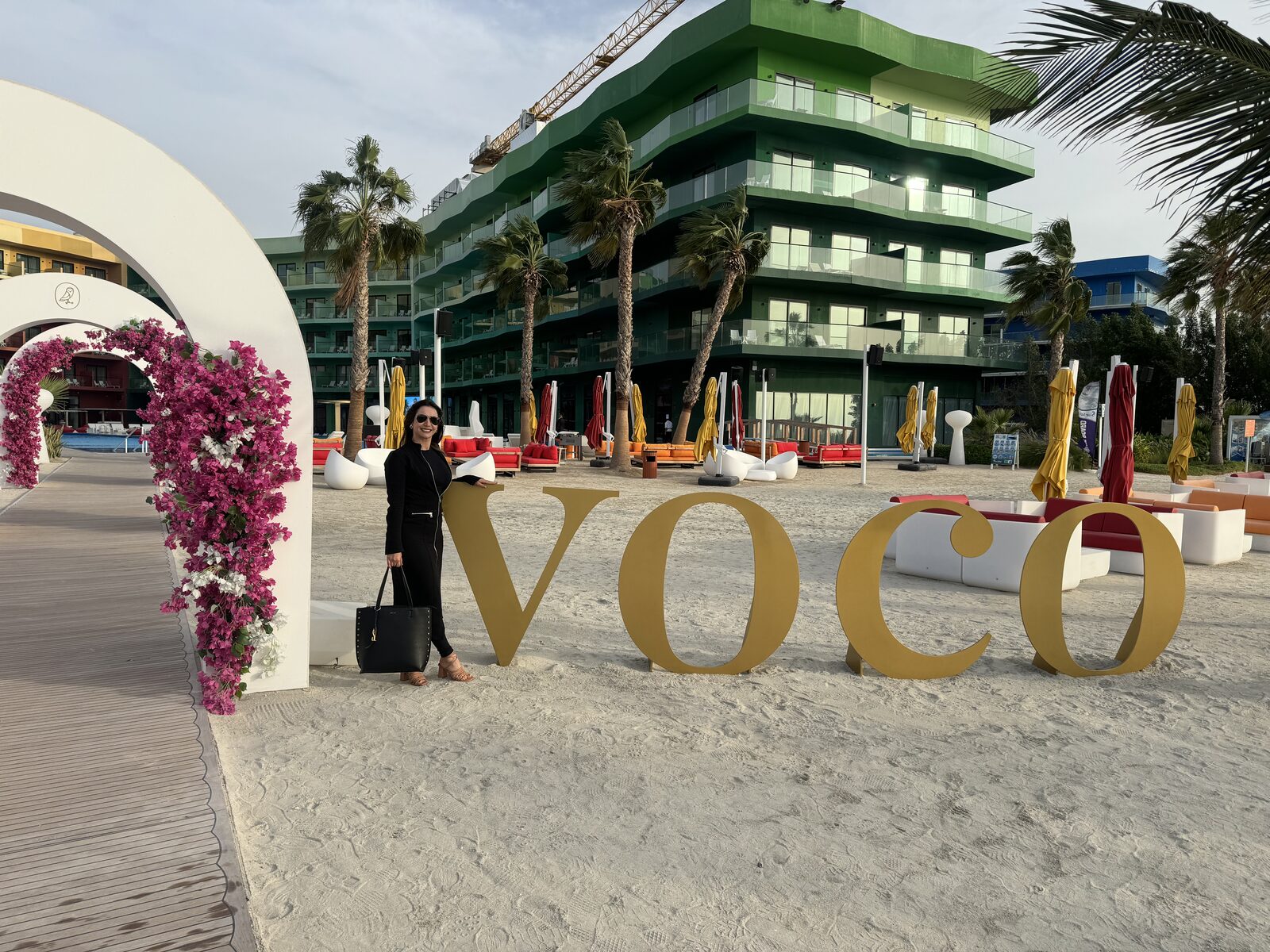 Esposa de Joaquim posando ao lado de letras gigantes formando a palavra VOCO, numa praia